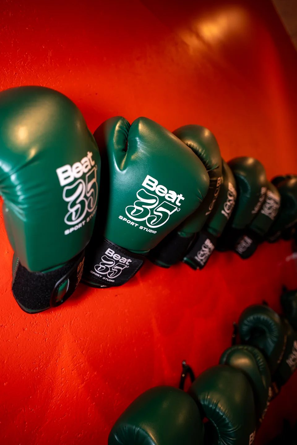 Gants de boxe verts Beat 35 rangés sur un mur orange